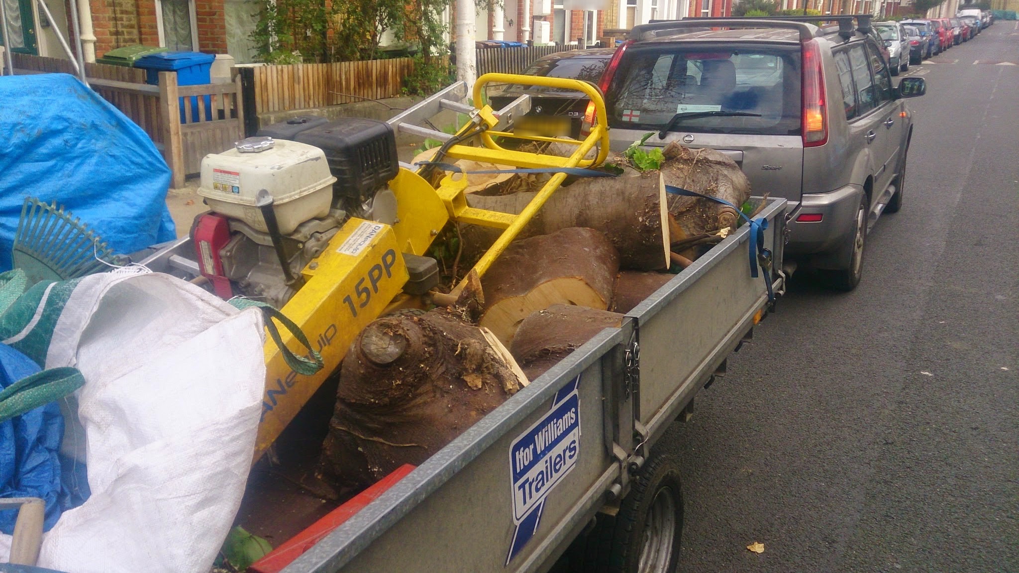 A trailer loaded with a yellow stump grinder, ground-out stumps and bags of waste